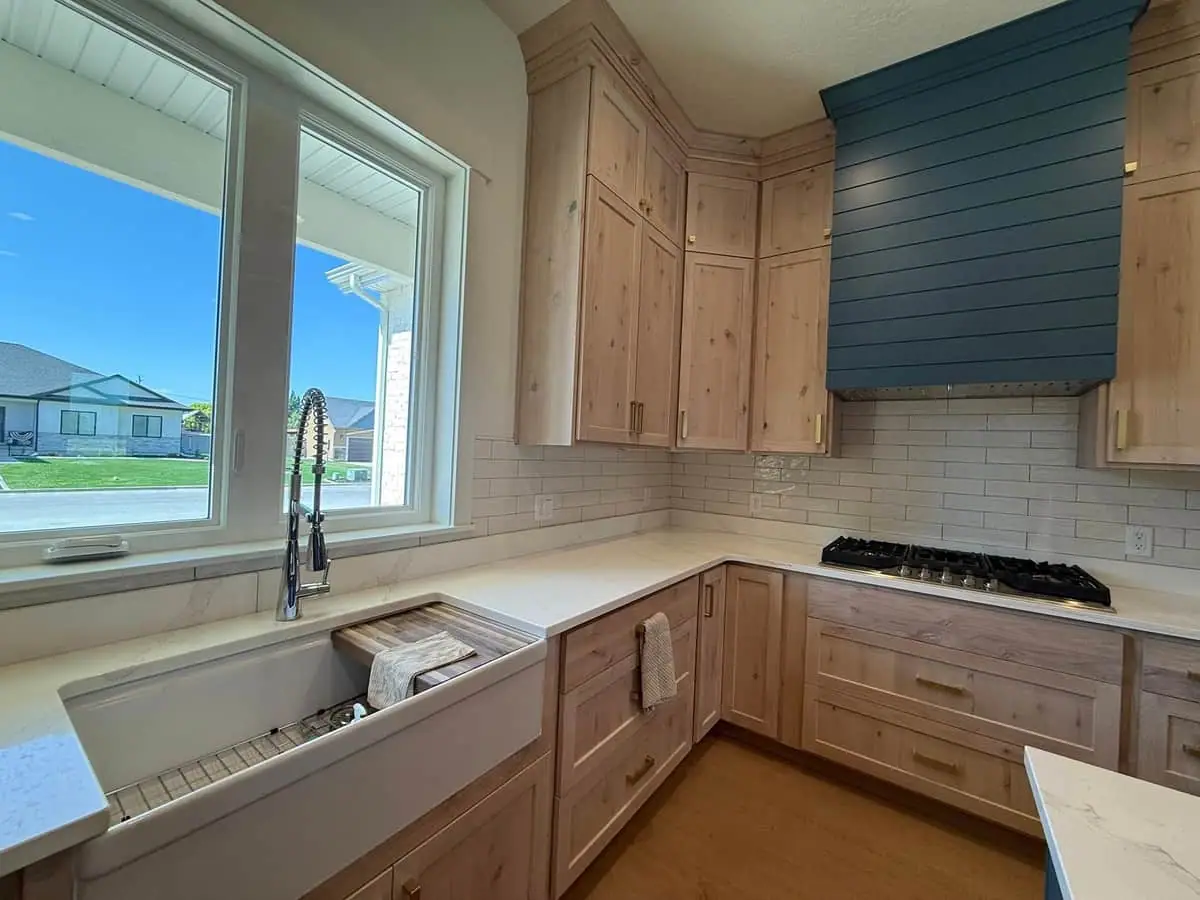 Kitchen with light wood cabinets, farmhouse sink, and blue shiplap hood